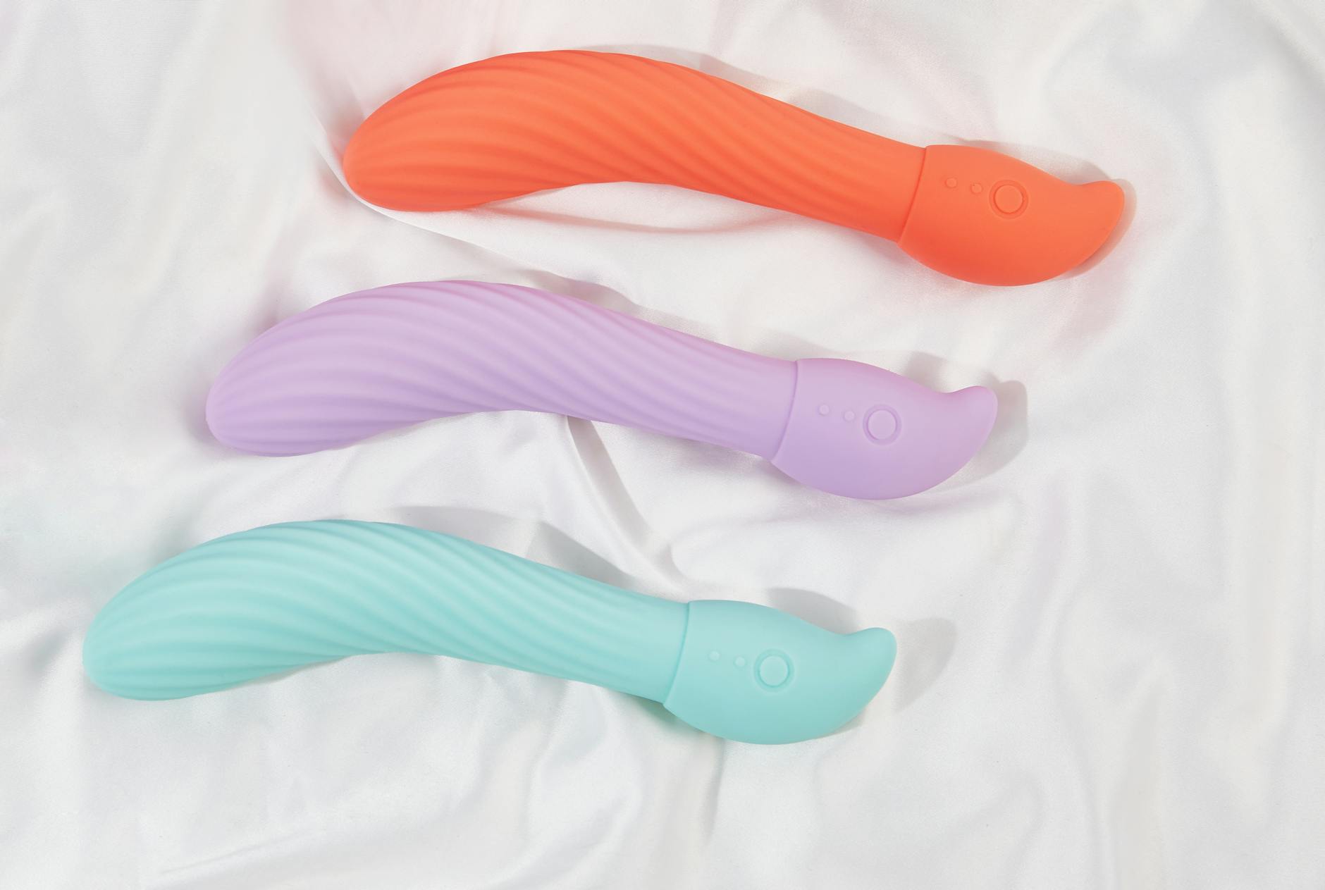 Three colorful silicone vibrators arranged on white fabric, showing smooth texture and design detail.