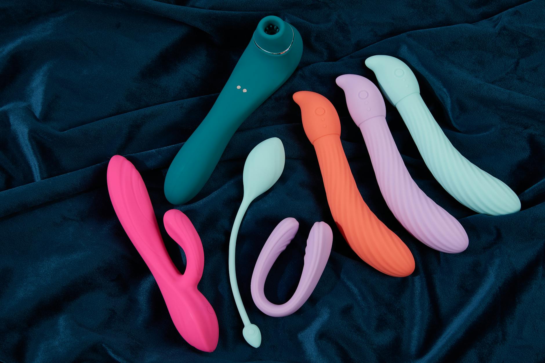 Array of colorful clitoral vibrators and adult toys displayed on silk fabric