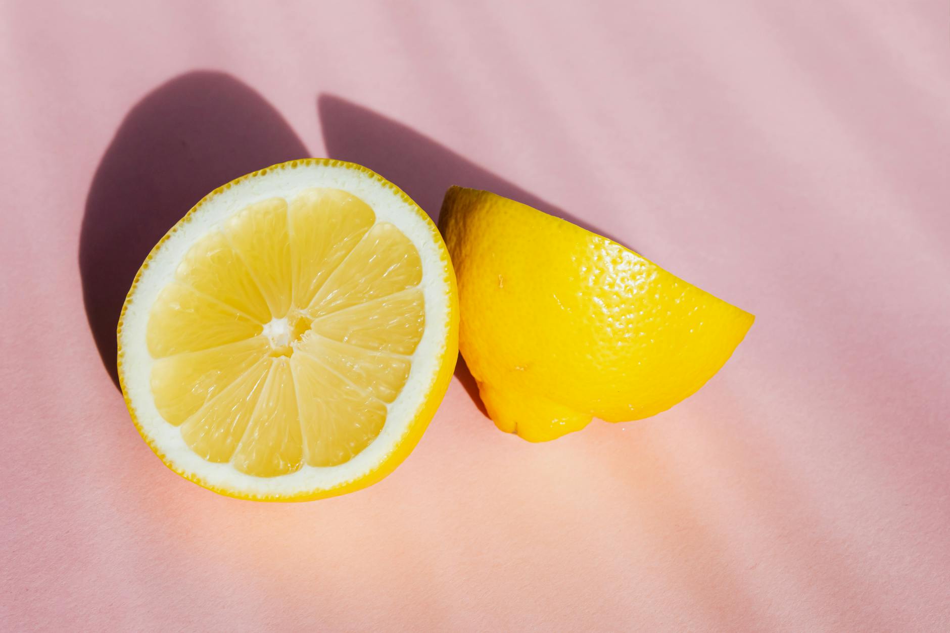 Fresh lemon halves on a pink background in natural light, symbolizing the Lem vibrator by Hello Nancy