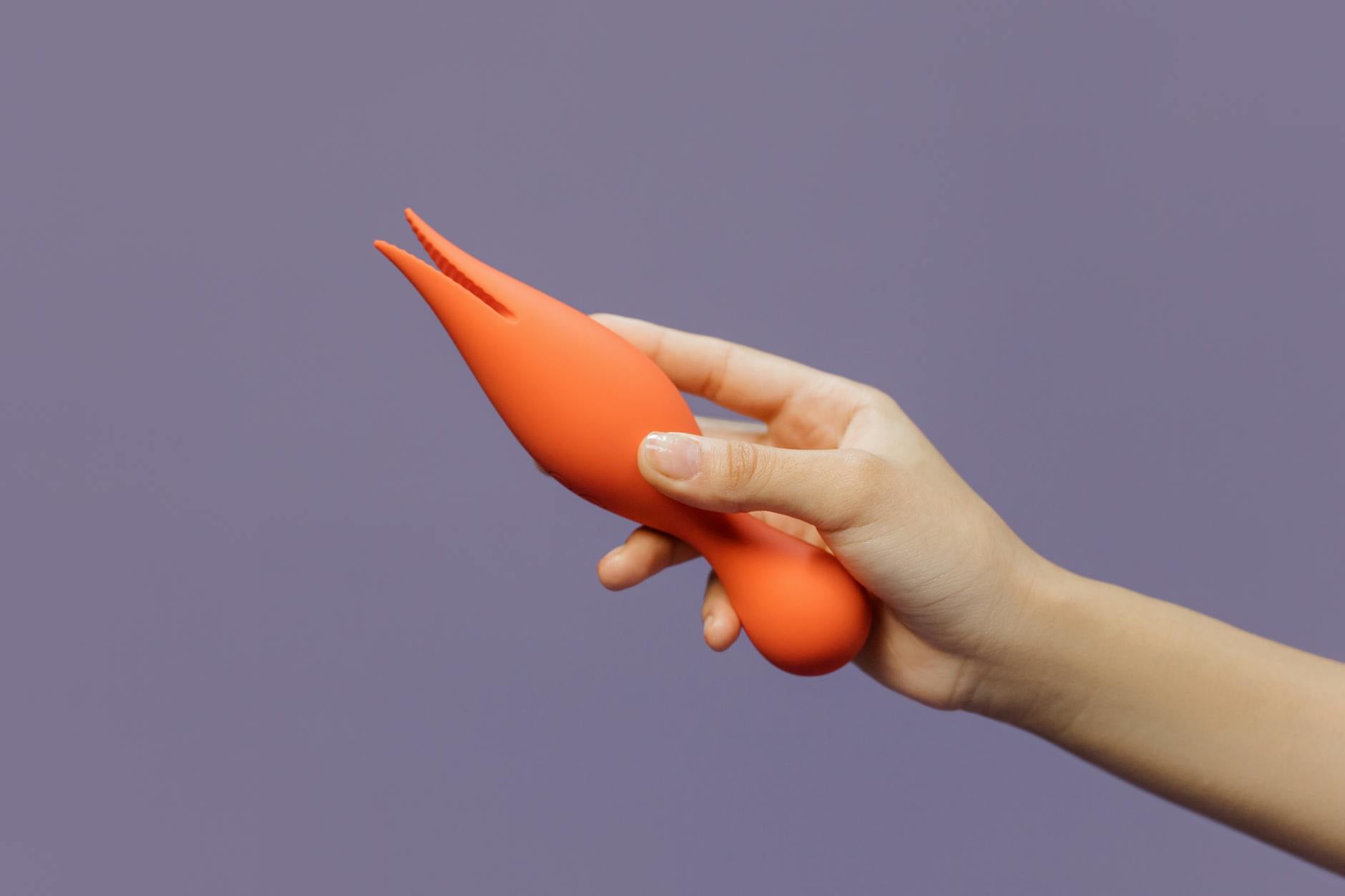 Hand holding a lemon clitoral vibrator against a minimalist purple backdrop