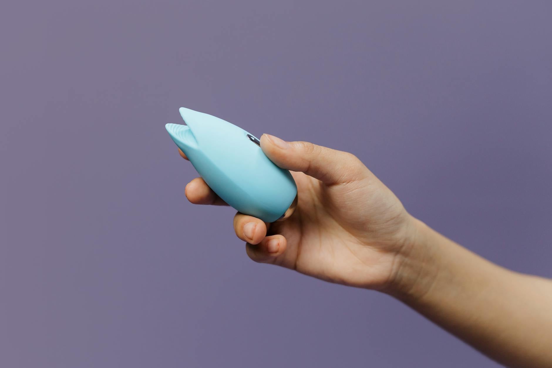 Woman holding two colorful vibrators against purple background showing self-pleasure options