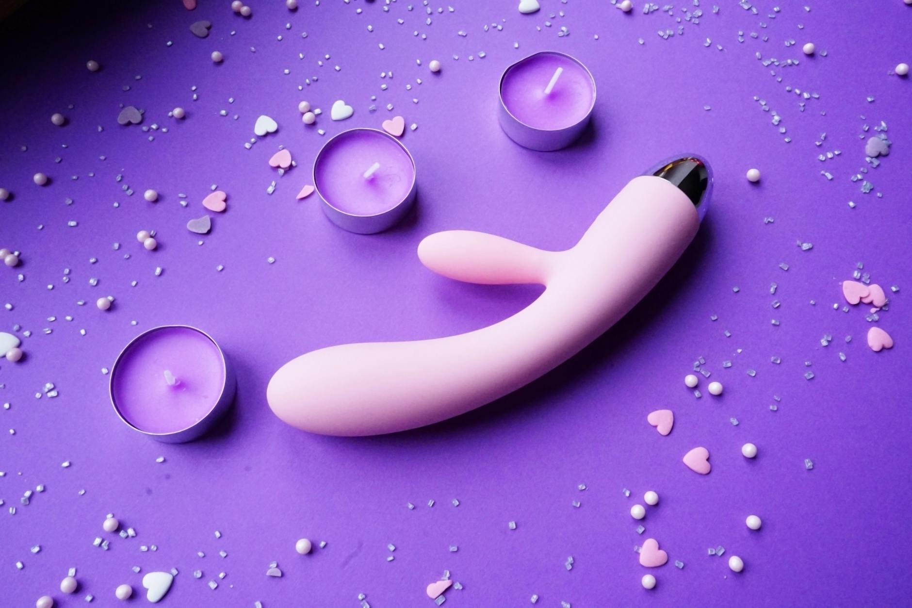 Colorful vibrators displayed with flowers in a holographic gift bag against a yellow background